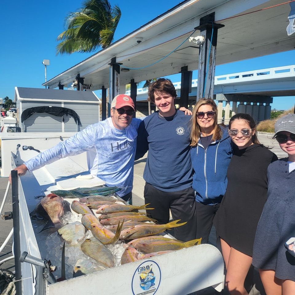 Five people stand smiling beside a boat cleaning station filled with a variety of freshly caught fish on ice.