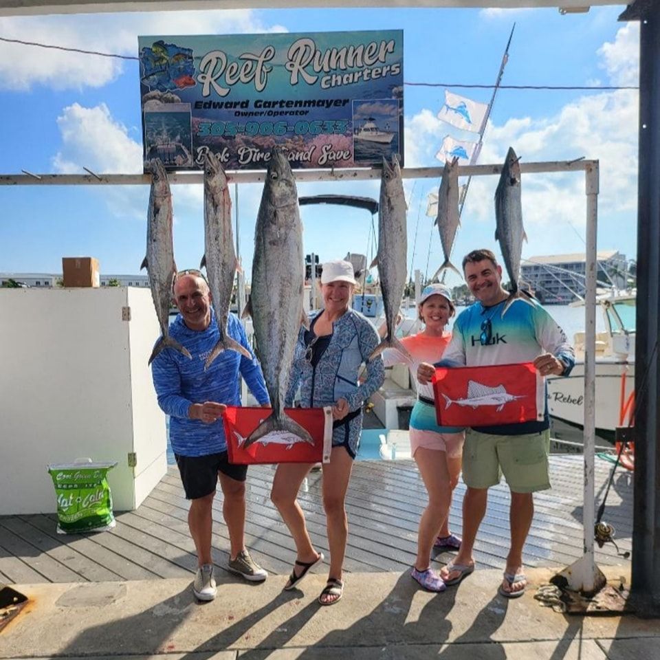 Four people standing on a dock holding fish caught on a Reef Runner charter trip, with a sign hanging above.