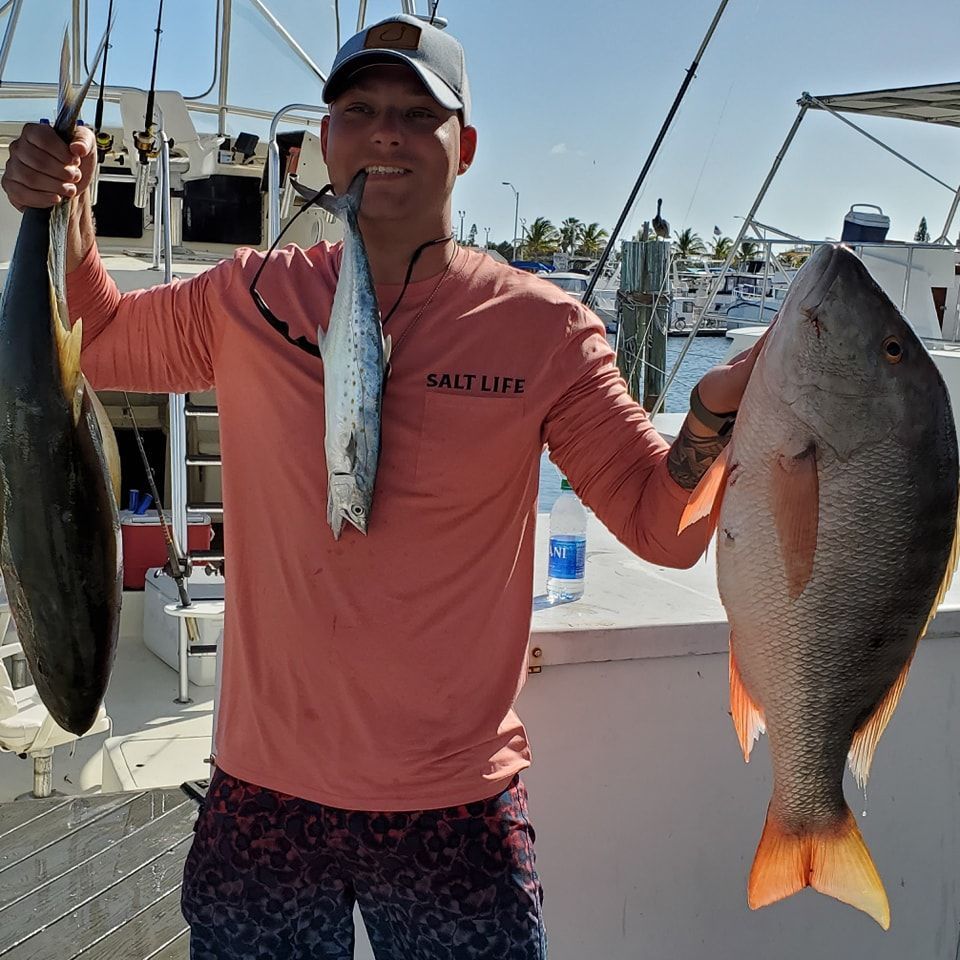 A person wearing a peach long-sleeve shirt stands on a boat holding three fish of varying sizes.