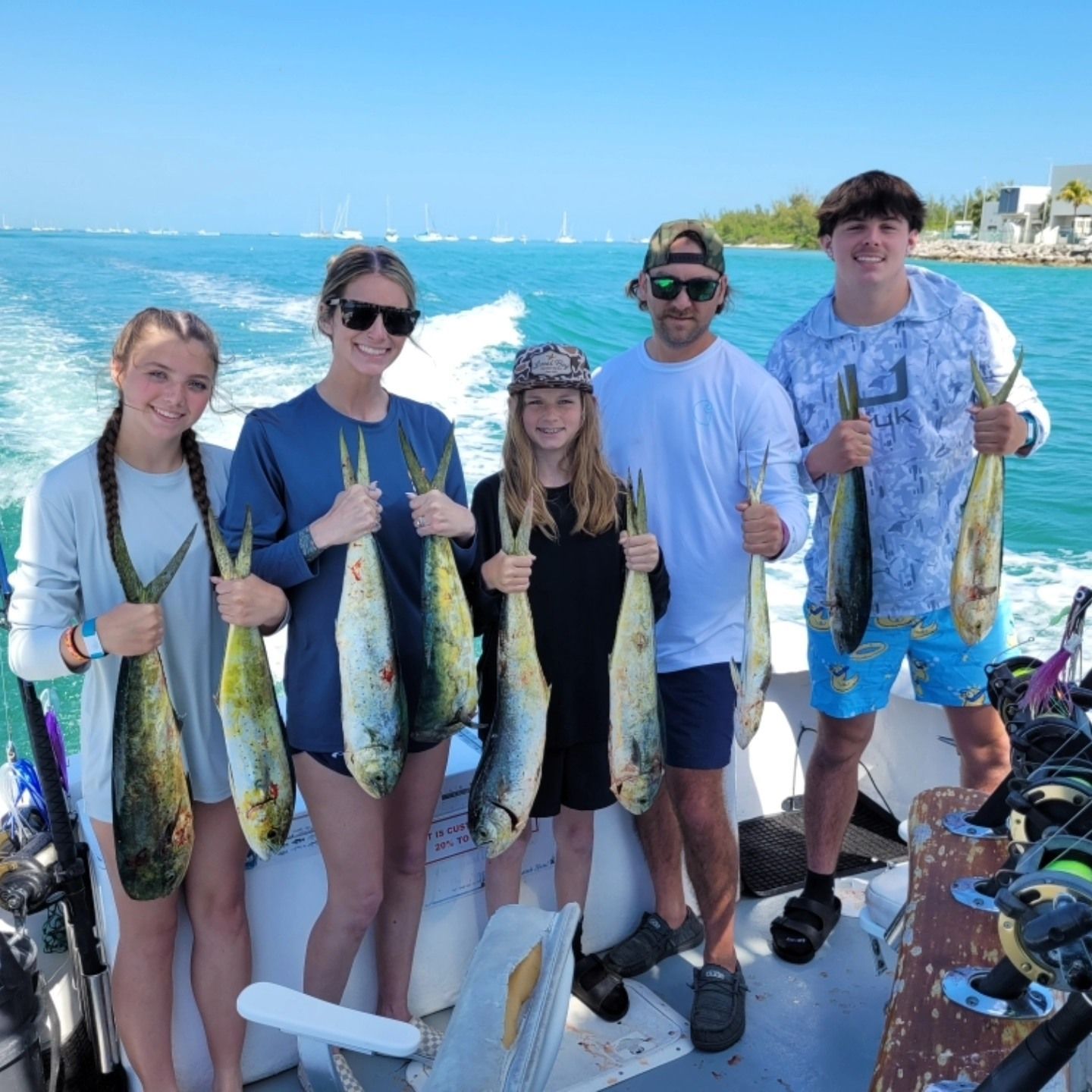 Five people on a boat in sunny, blue waters holding freshly caught mahi-mahi fish.