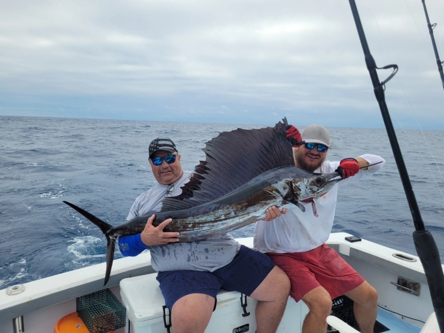 Two people on a boat hold a large sailfish up for a photo in the middle of the ocean.