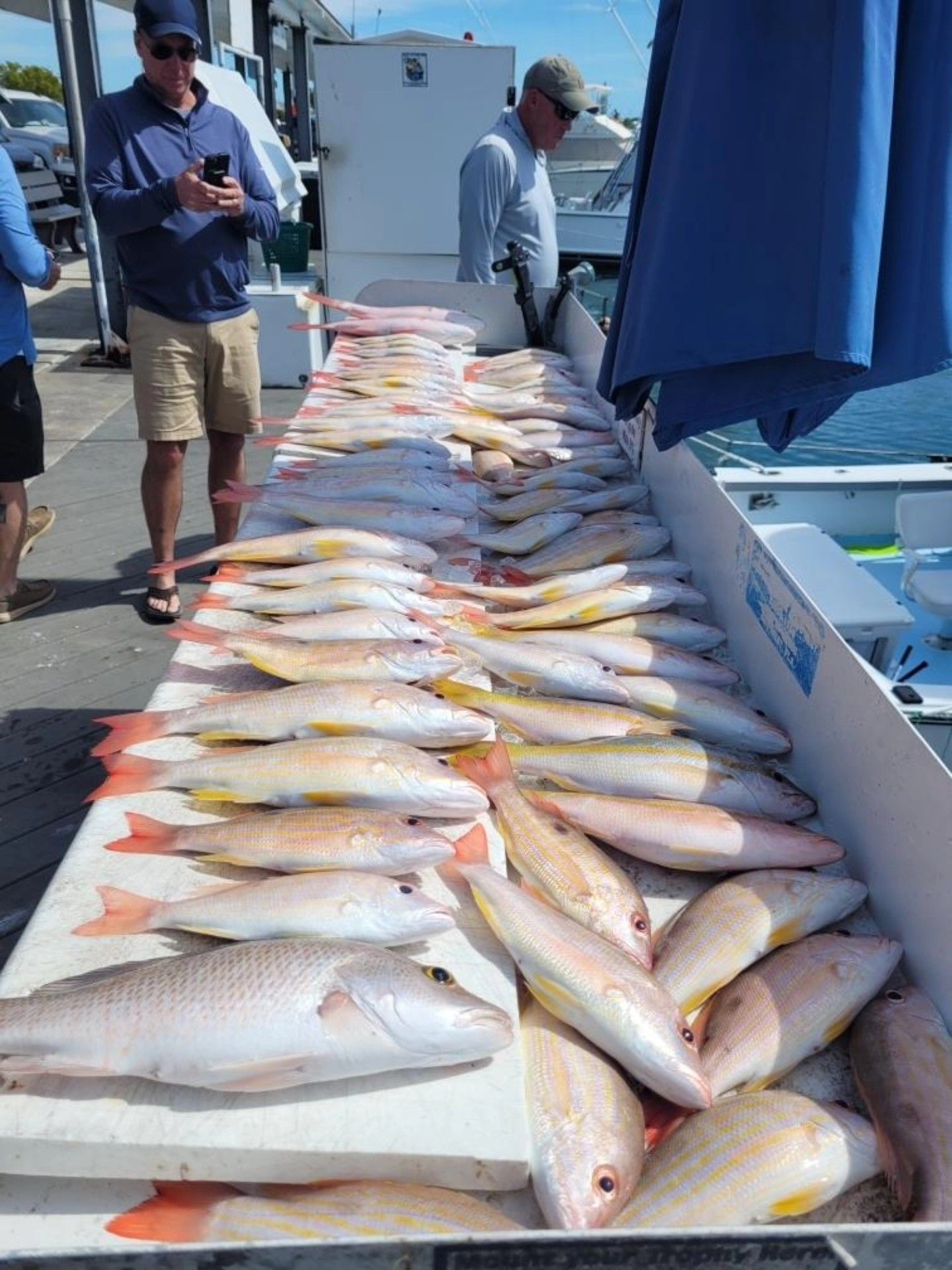 Two people stand at a cleaning station with a large catch of fresh fish spread out on a white surface at a dock.