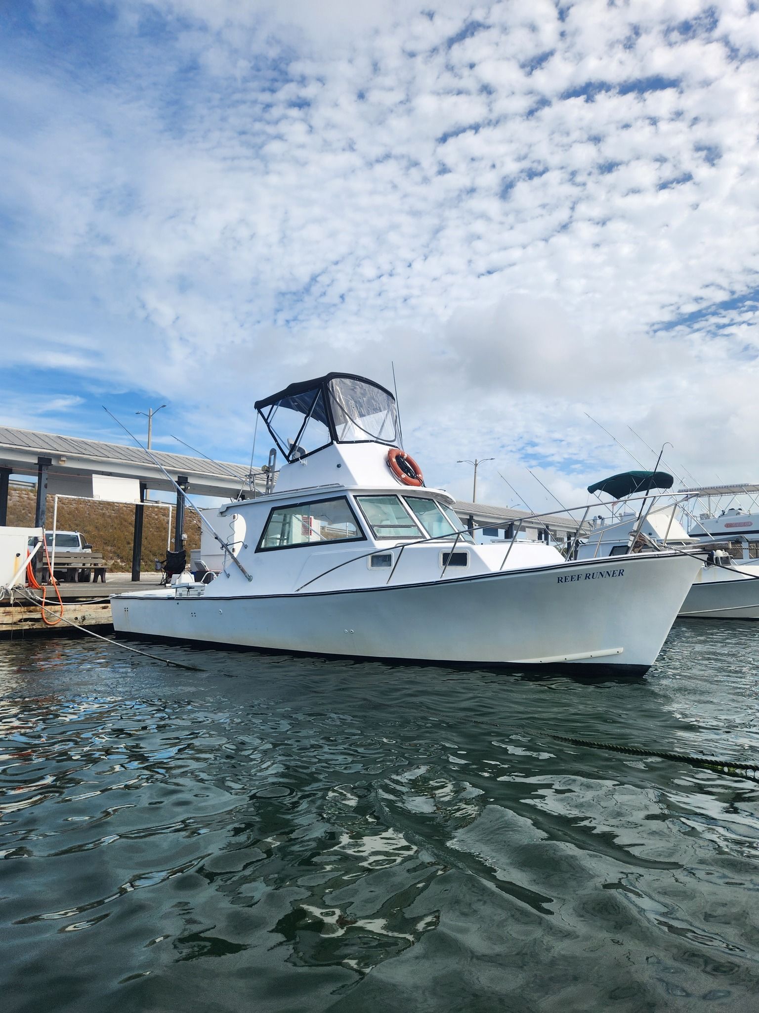 A white motorboat docked at a harbor under a bright, cloudy sky.