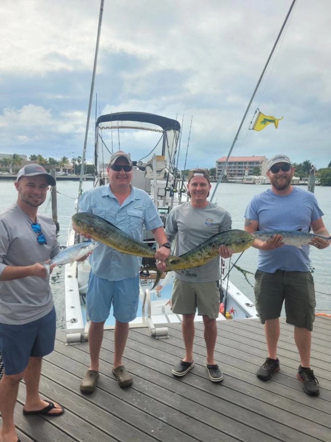 Four people stand on a dock in front of a fishing boat, holding mahi-mahi and other smaller fish after a day on the water.