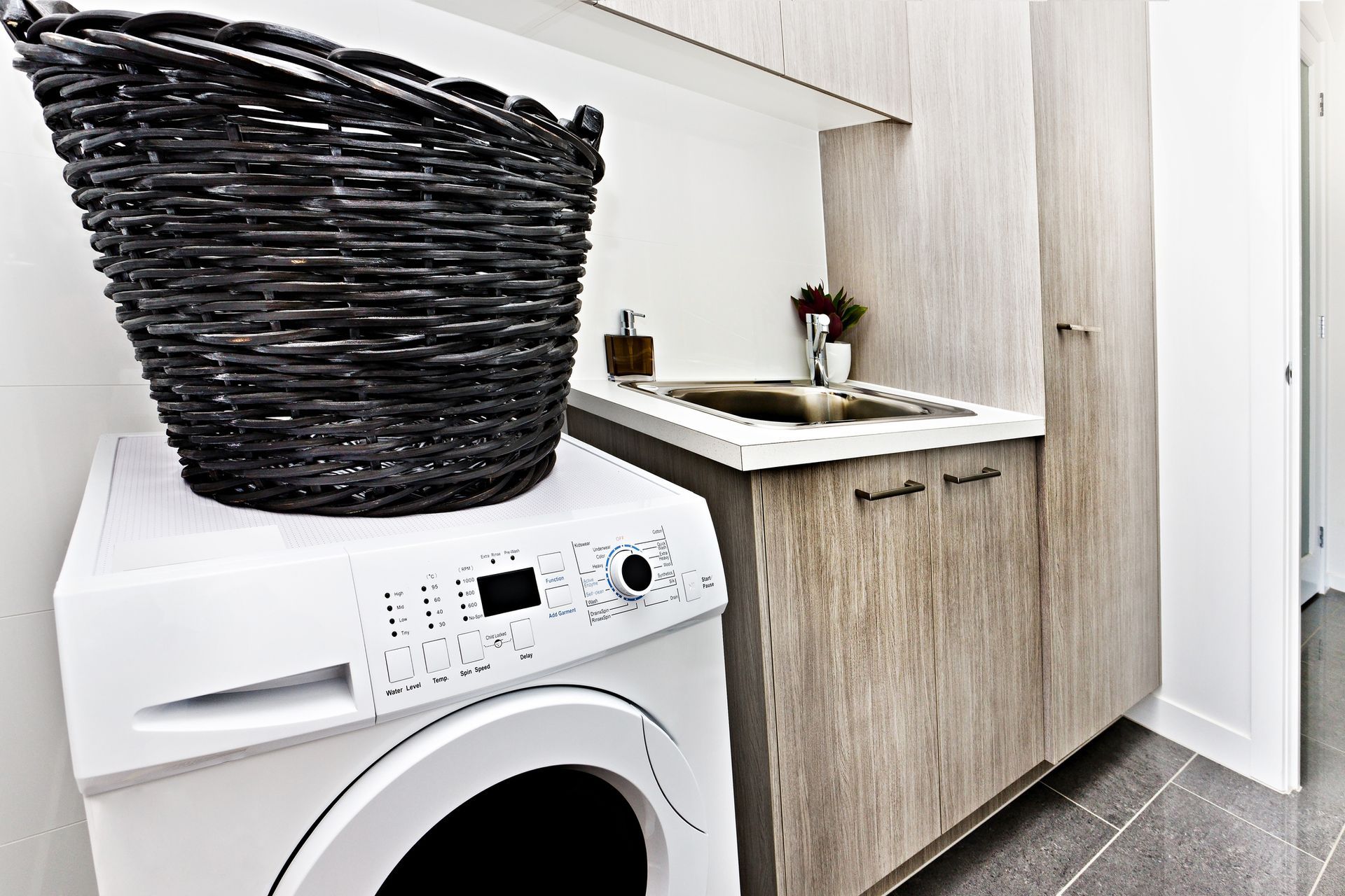 A laundry room with a washing machine, a black basket on top, and a sink with cabinets.