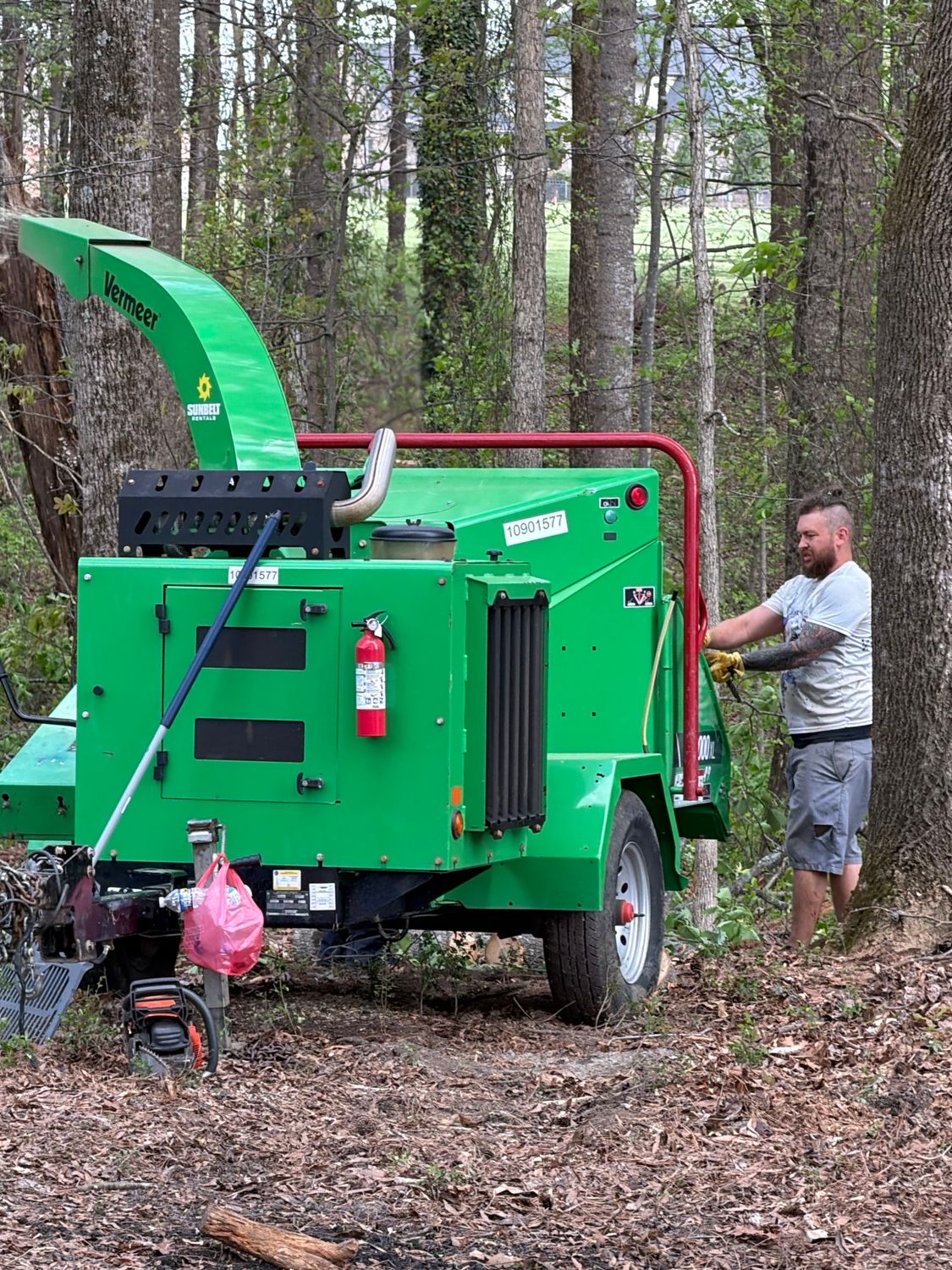 Green wood chipper in forest as a man feeds branches into it