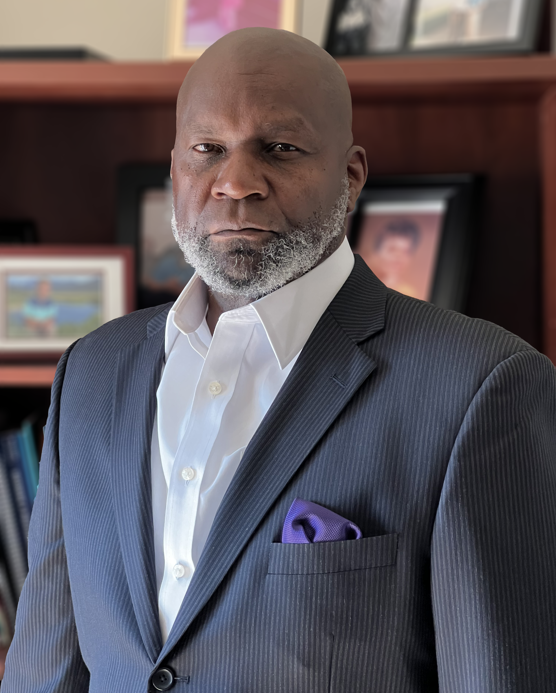 A man in a suit and white shirt is standing in front of a bookshelf.
