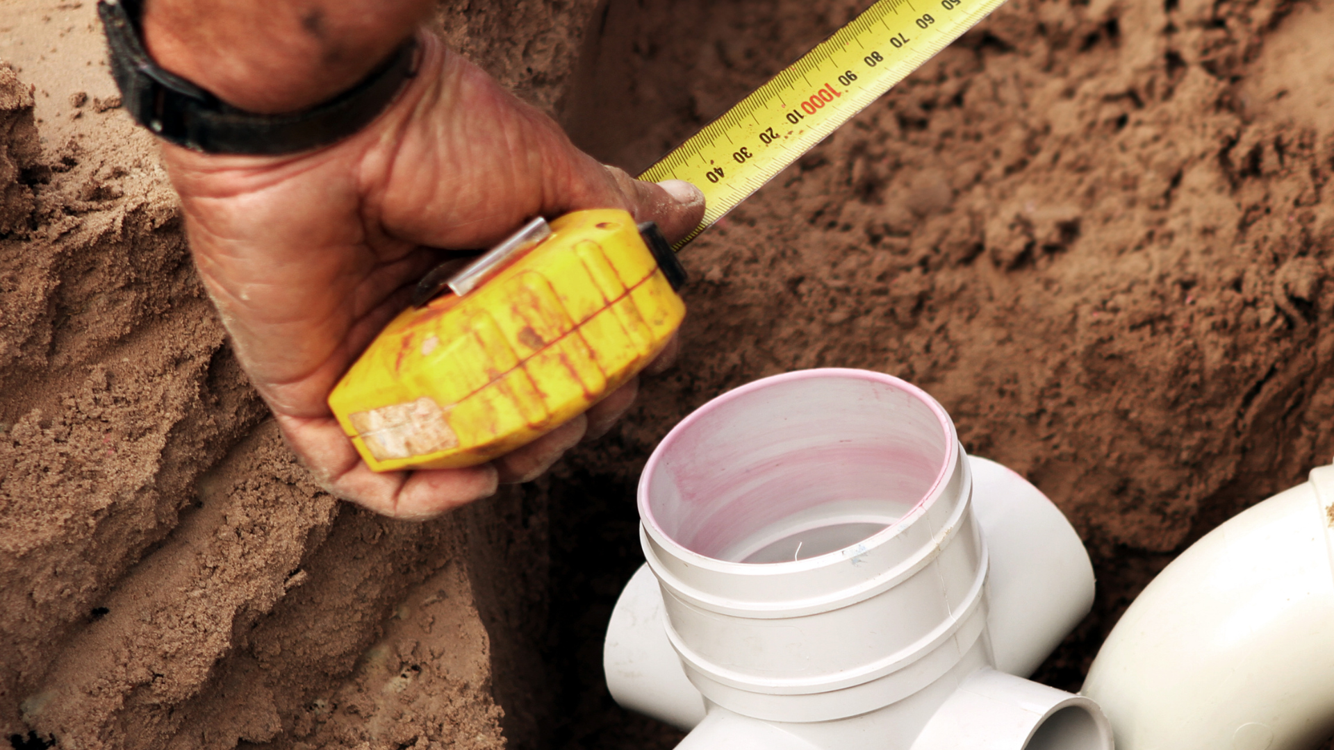 A person is measuring a pipe with a tape measure.