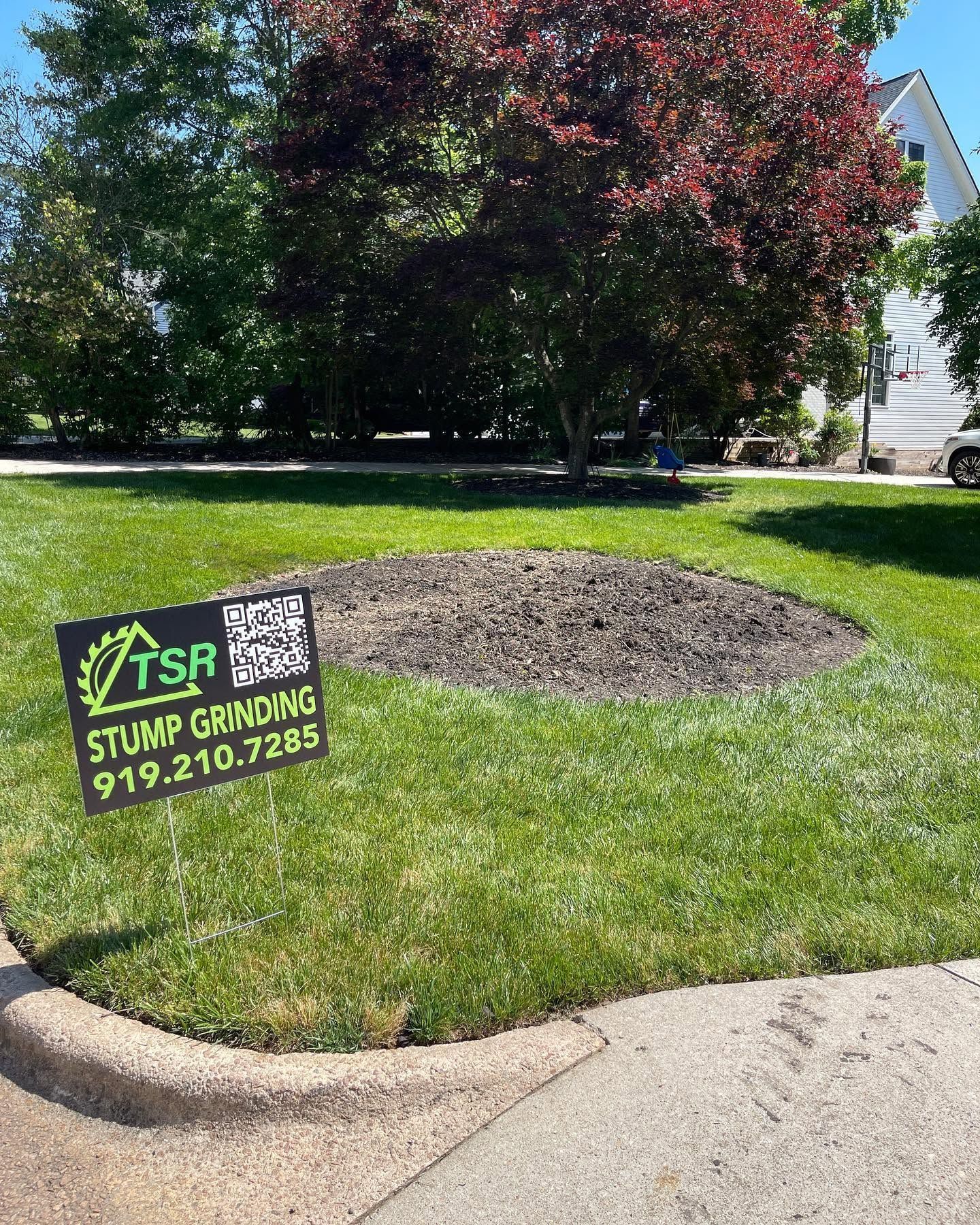 Front yard with a tree stump and fresh mulch, lawn sign for T&R Stump Grinding in a suburban yard.