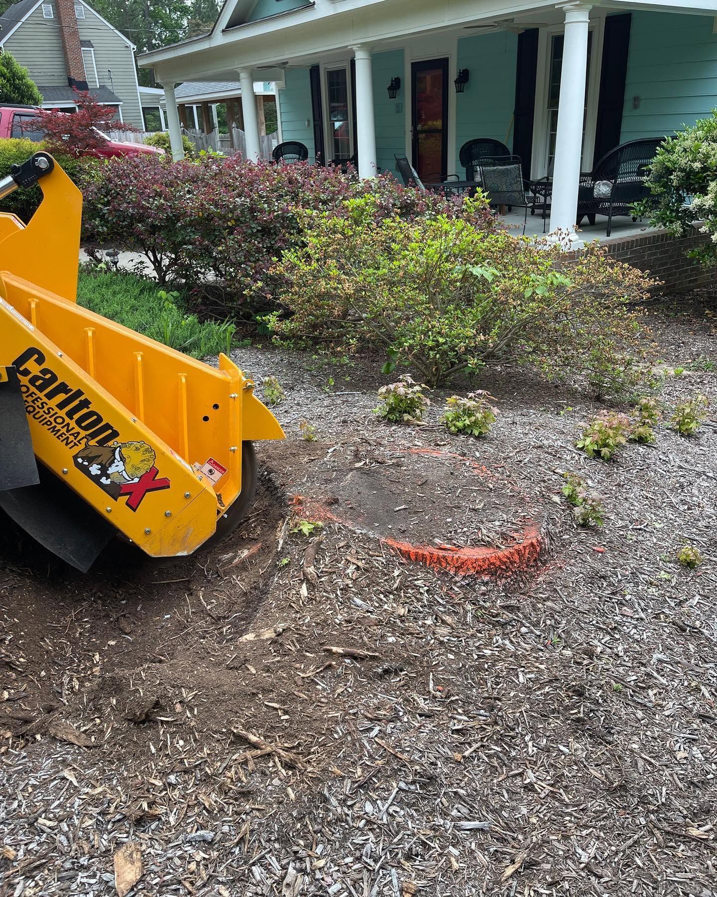 Yellow construction machine near mulch bed beside a house porch