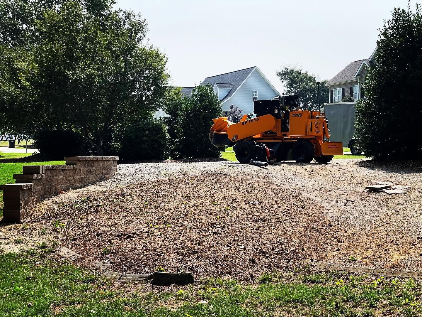 Orange utility truck on a gravel driveway beside a brick wall and trees in a sunny yard