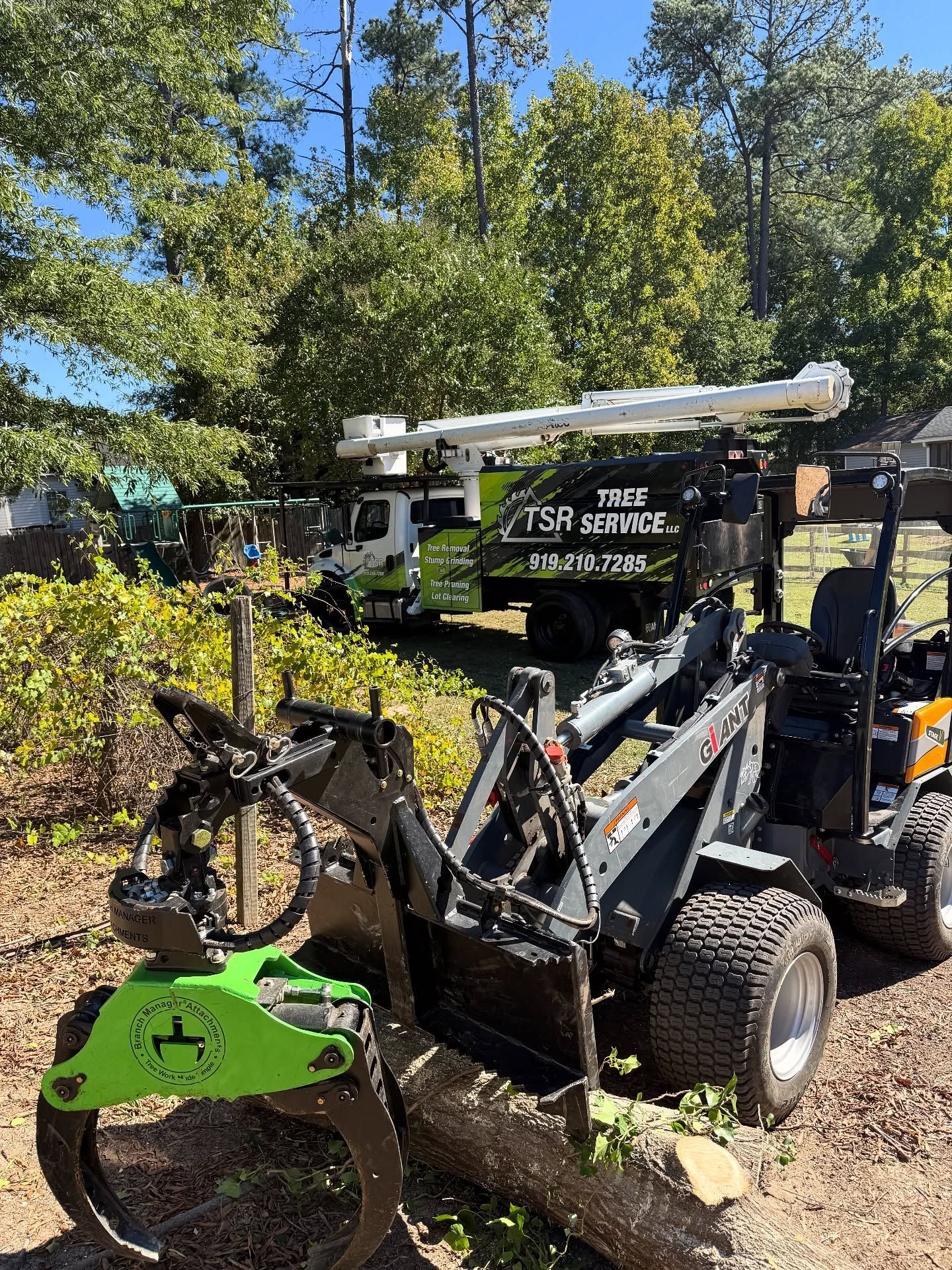 Black utility lift truck with green mower attachment parked outdoors among trees and brush.