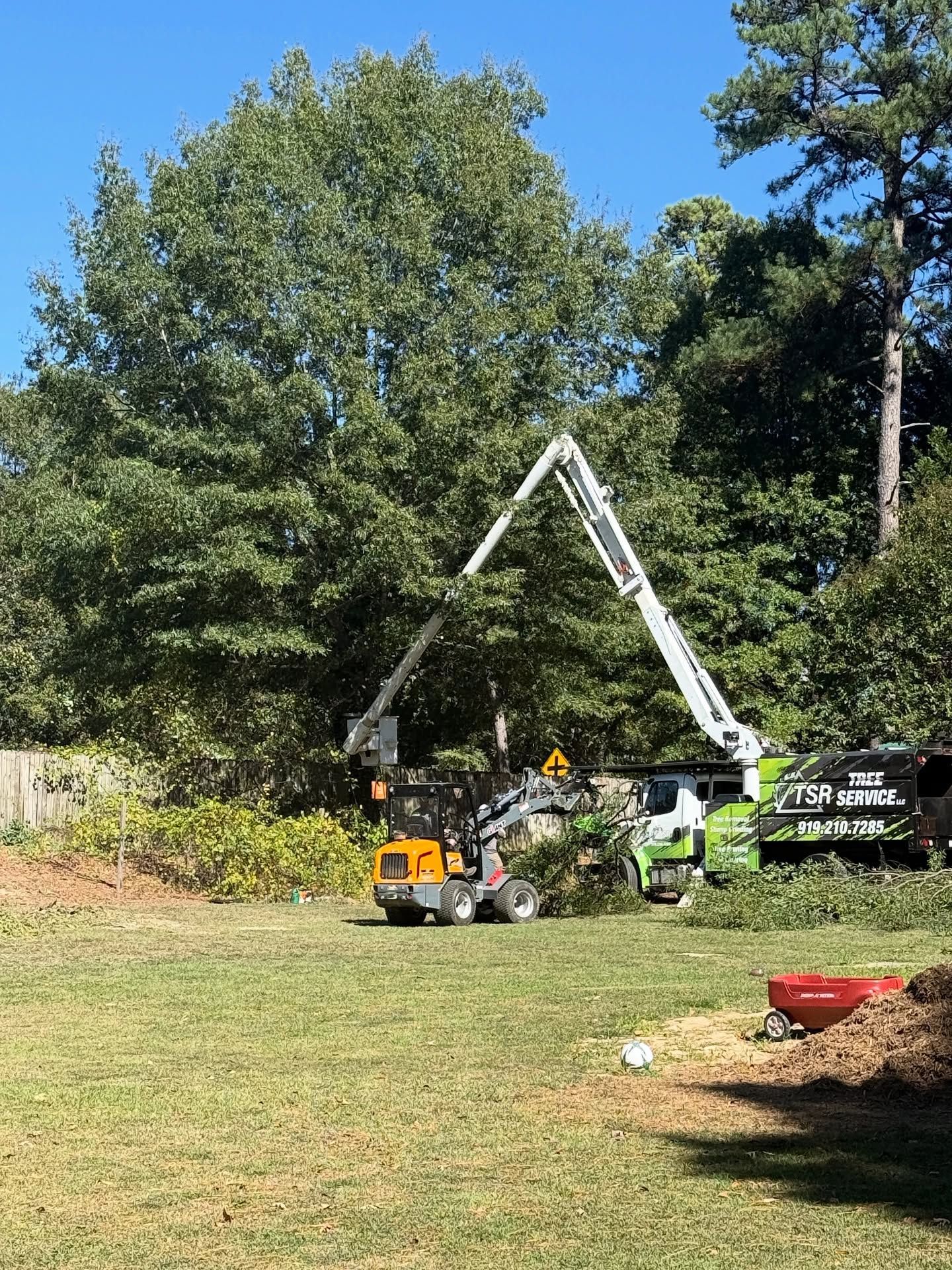 Two workers using a crane to lift a white A-frame structure in a grassy yard