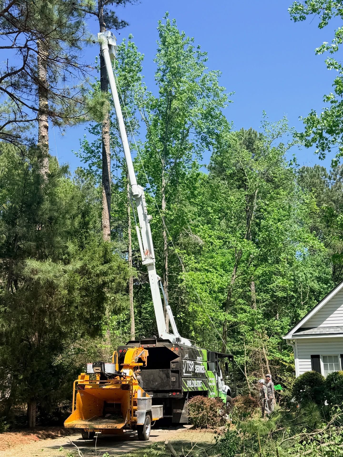 Utility truck lifting tree branches beside a house in a wooded yard