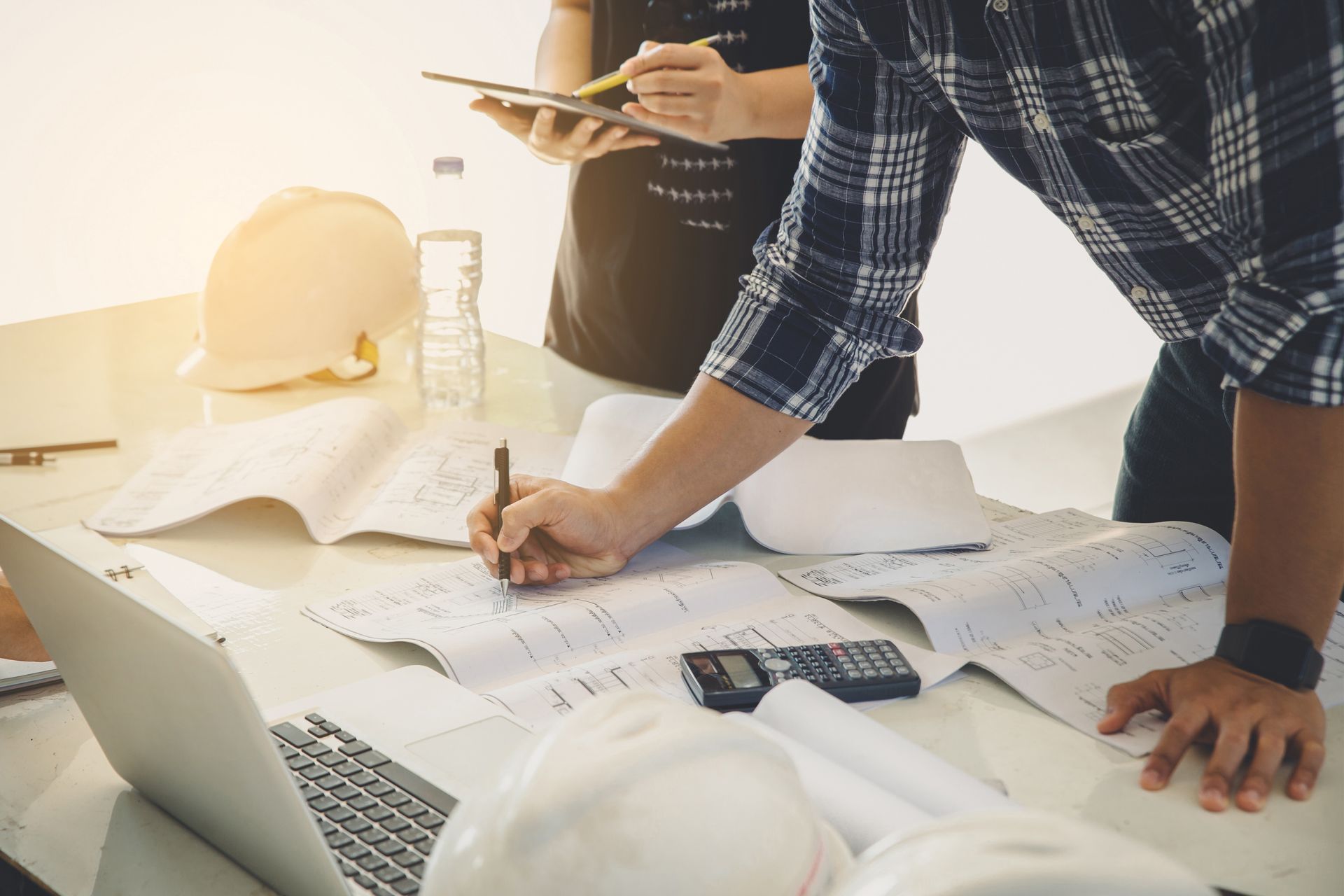 Two people working on architectural or engineering plans spread across a table Two people working on architectural or engineering plans spread across a table