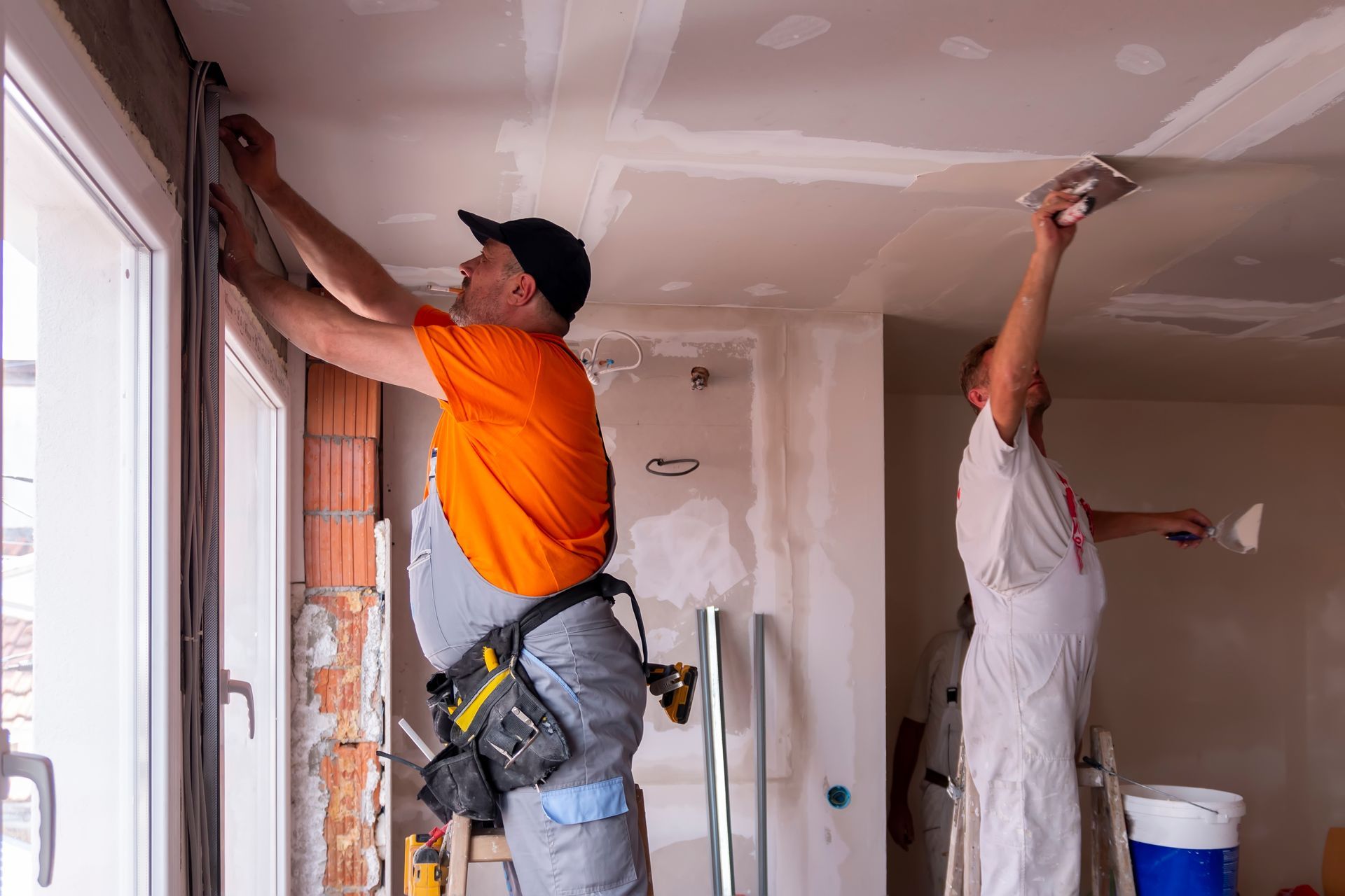 Contractors applying drywall joint compound to ceiling and wall seams during interior renovation Contractors applying drywall joint compound to ceiling and wall seams during interior renovation