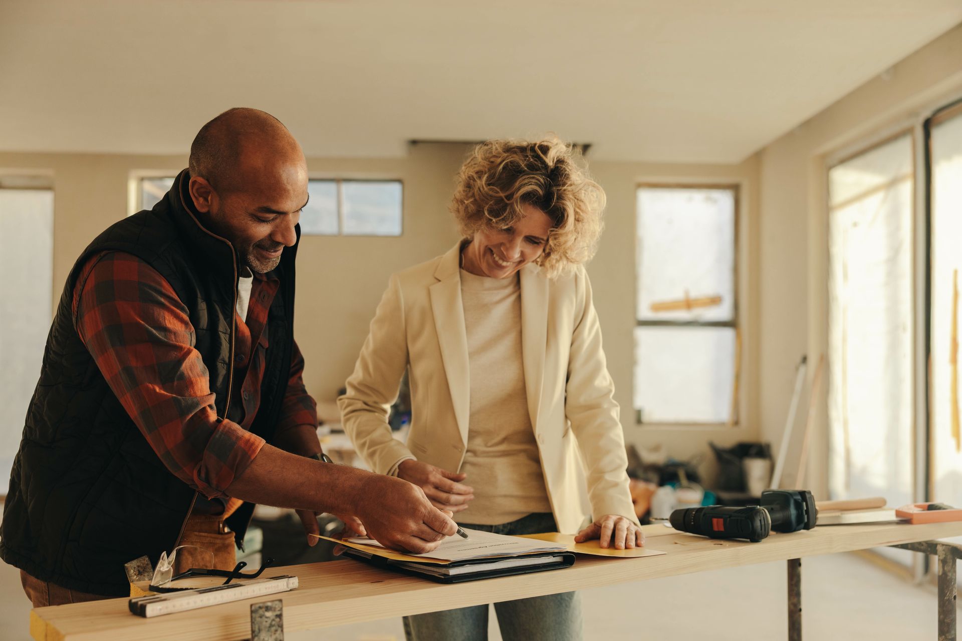 A contractor and a homeowner reviewing renovation plans together at a job site work table A contractor and a homeowner reviewing renovation plans together at a job site work table