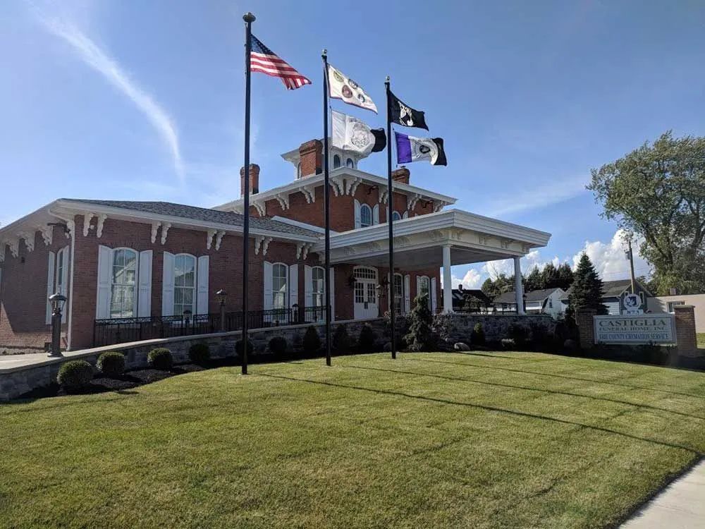Brick civic building with four flagpoles and a manicured lawn under a clear blue sky