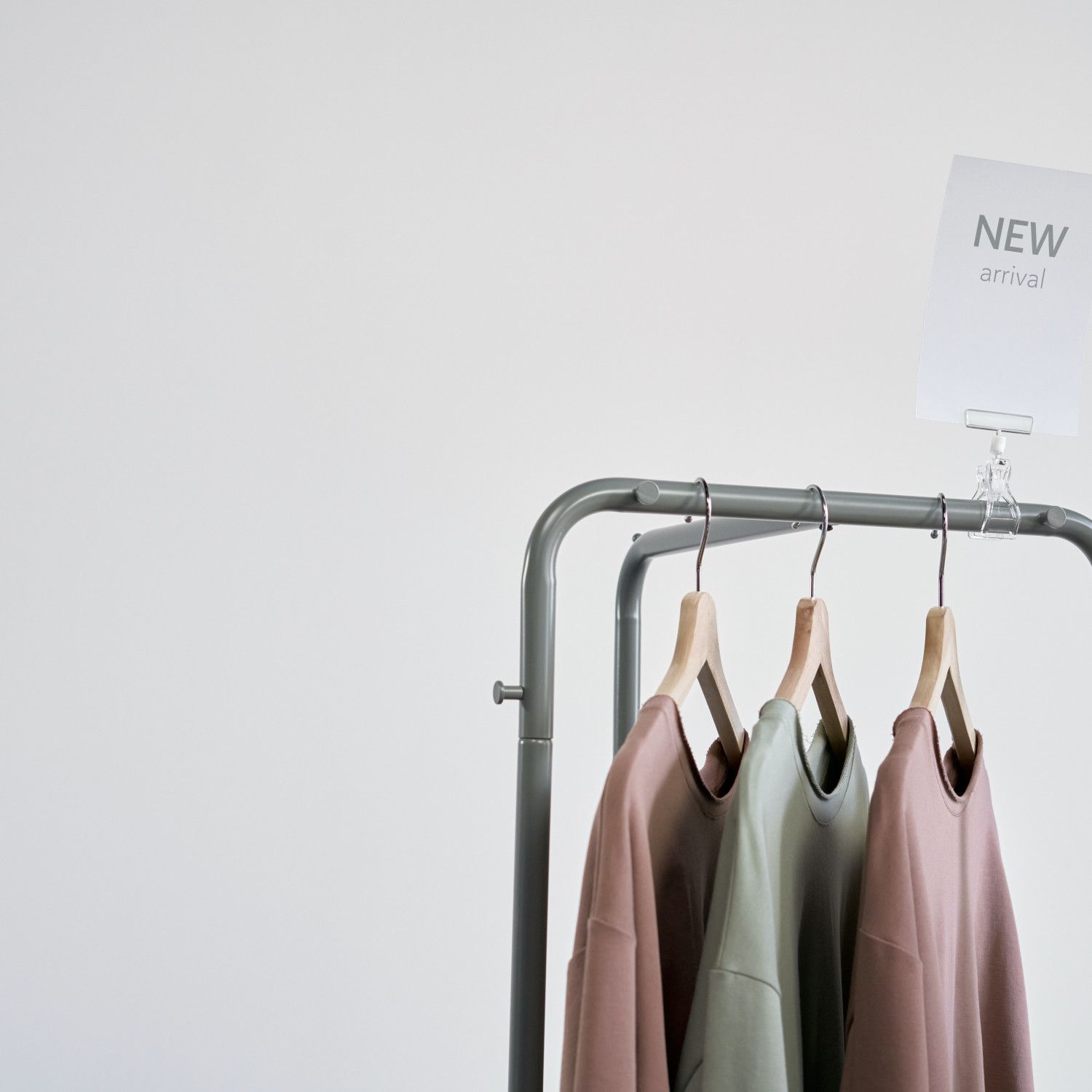 Three neutral-toned jackets on hangers on a clothing rack with a small