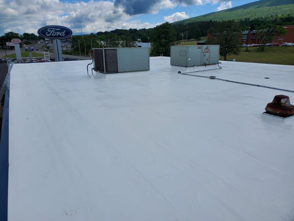 Rooftop with white membrane roof, HVAC units, and a Ford sign in the background under cloudy sky