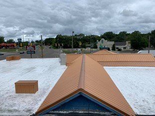 Rooftop with tan metal ridge vents under a cloudy sky, surrounded by trees and houses.