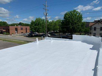 White flat roof under a blue sky, with a utility pole, trees, and buildings in the background
