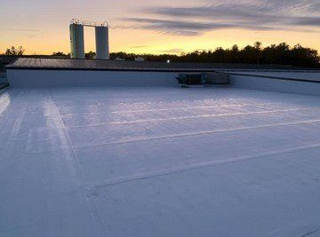 White flat rooftop at sunset with two vents and a small unit against a dark tree line