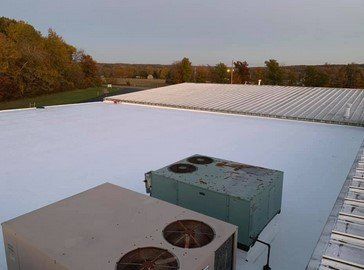Rooftop HVAC units on a flat white commercial roof beside trees at dusk