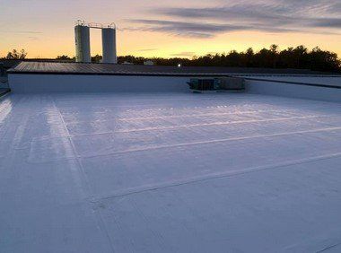 Flat white rooftop at sunset with two chimneys and a low vent in the distance