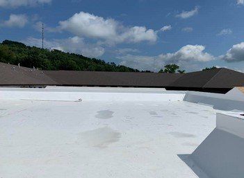 White flat rooftop with dark trim under a blue sky with clouds and green hills in the background