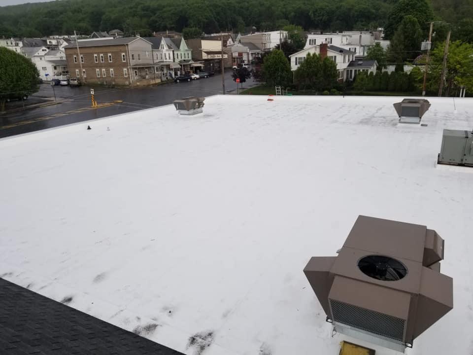 Snow-covered flat rooftop with vents, overlooking houses and trees under an overcast sky