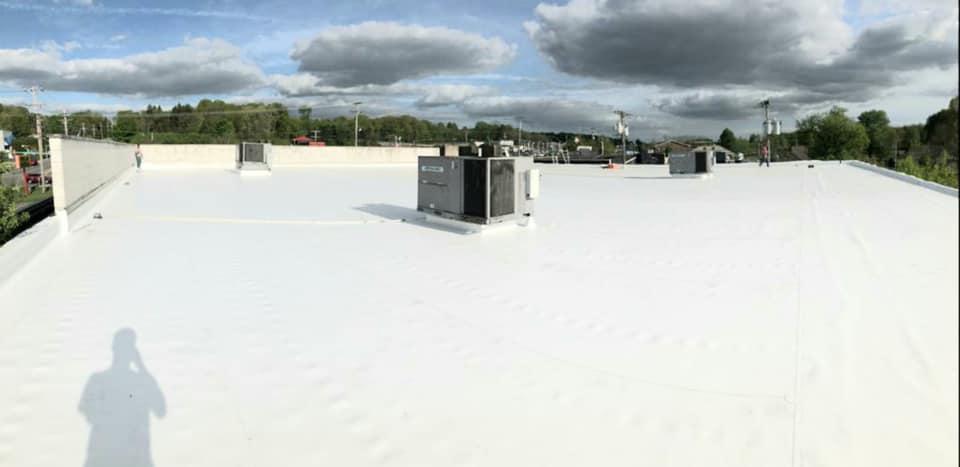 White flat rooftop with HVAC units under a cloudy sky, with a person’s shadow in the foreground