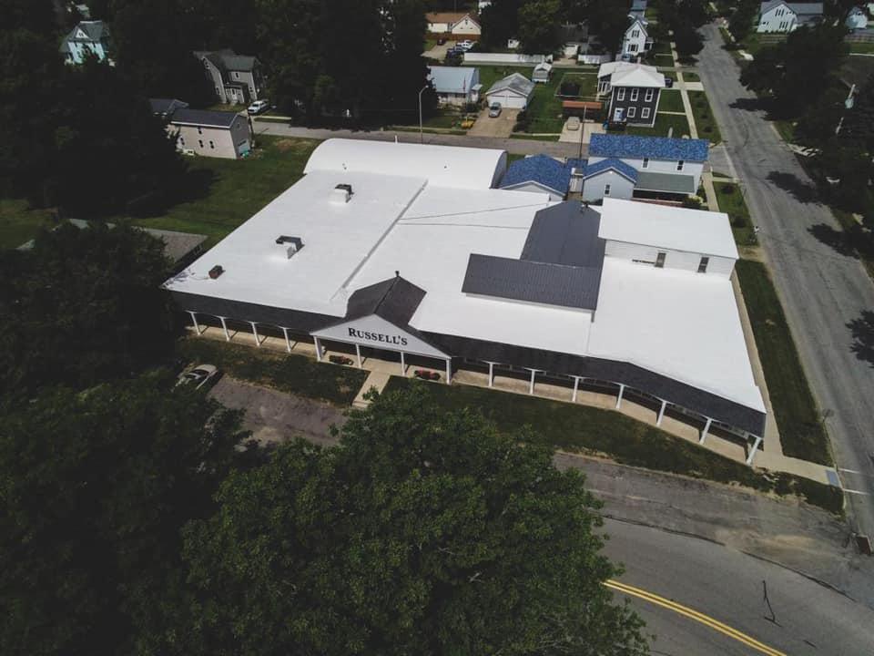 Aerial view of a large white-roofed building beside a road and trees.