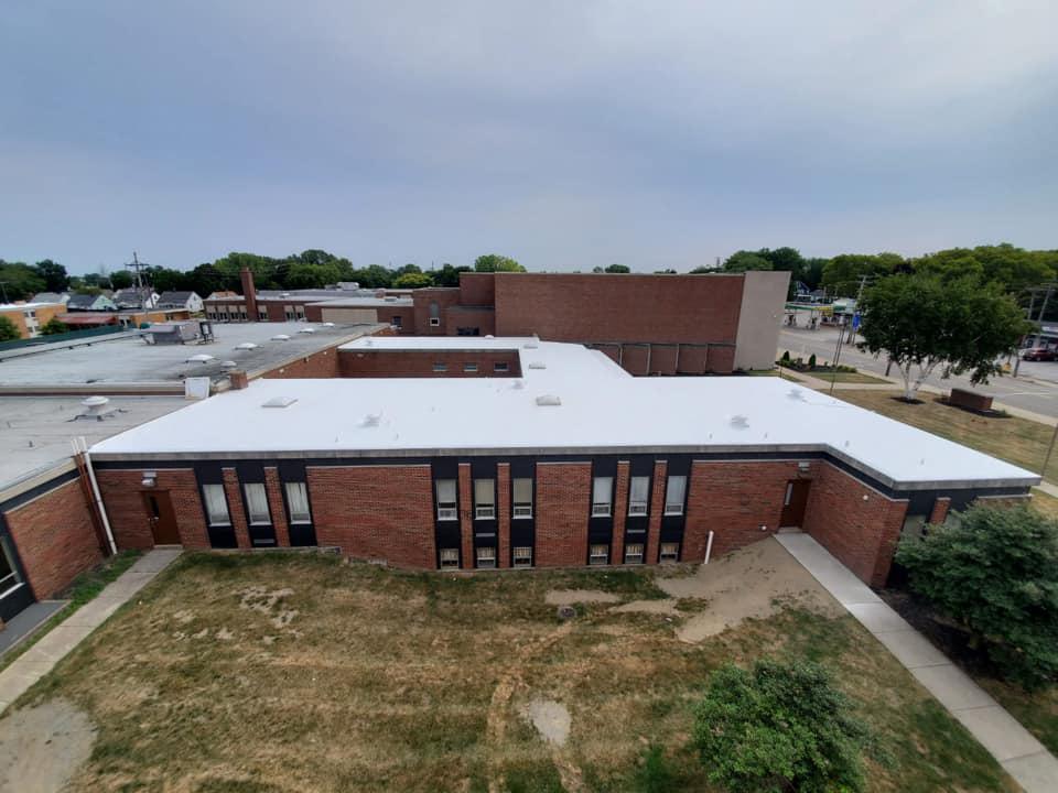 Aerial view of a brick school building with a white roof and surrounding trees.
