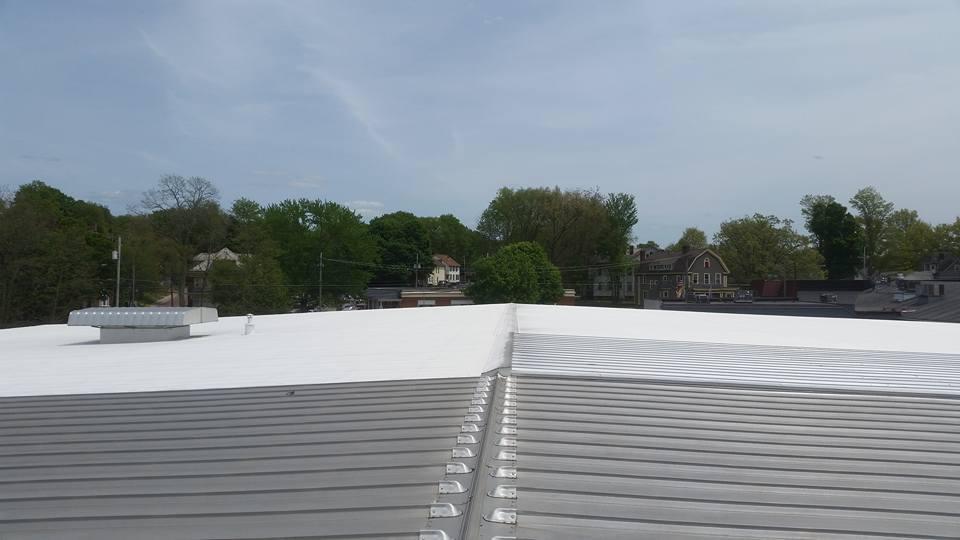 Rooftop with white and gray metal panels under a cloudy sky, trees in the distance.