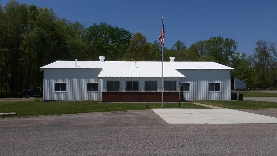 White single-story building with an American flag in front, surrounded by trees under a clear blue sky