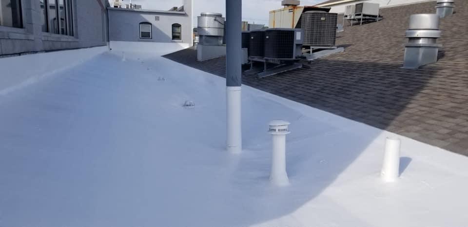 Snow-covered rooftop with vents and a nearby building wall under clear daylight