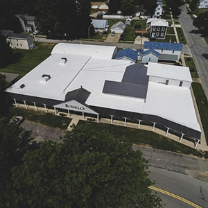 Aerial view of a large white-roofed building on a curved road in a residential area