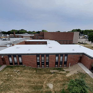 Aerial view of a red-brick school building with a white roof and grassy grounds