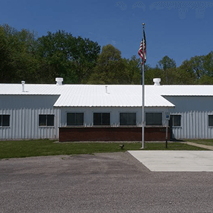 Single-story white building with a flagpole and American flag in front of a paved lot.