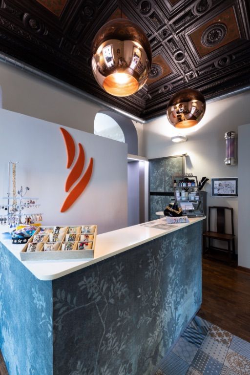 Banco della reception con logo arancione, lampade in rame e carta da parati a motivi.