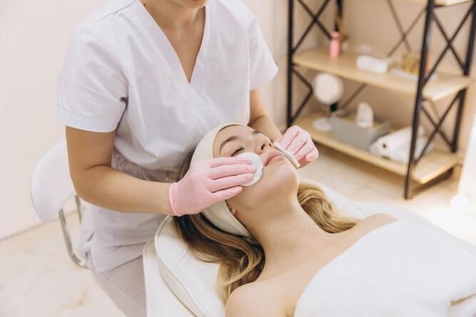 Persona che riceve un trattamento viso; estetista che pulisce il viso con dischetti di cotone.