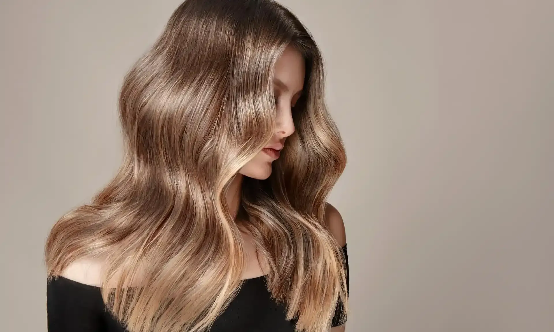 Donna con capelli lunghi, ondulati, castano chiaro, raccolti sulle spalle, su uno sfondo neutro.