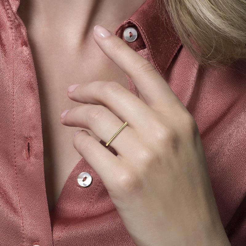 Een vrouw met een roze shirt en een gouden ring aan haar vinger