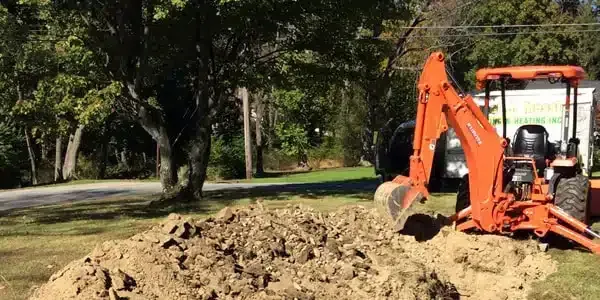 An orange excavator is digging a hole in the dirt in a yard.