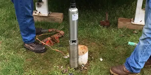 A man is standing next to a water pump in the grass.