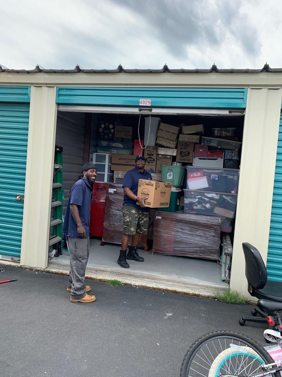 Two people moving boxes from a storage unit filled with packed items.