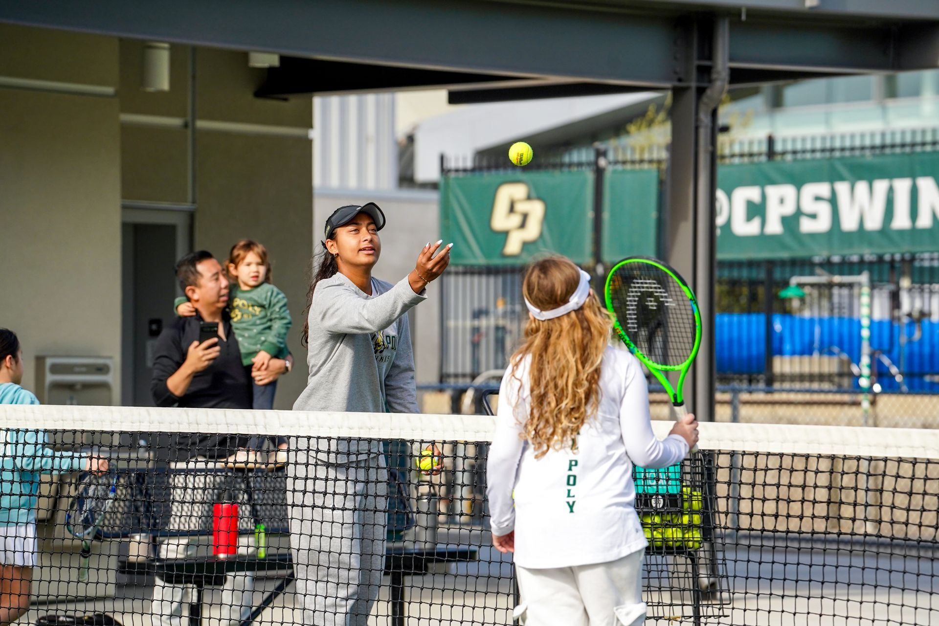 Tennis players and coach on a court beside the net, with one player holding up a racket.