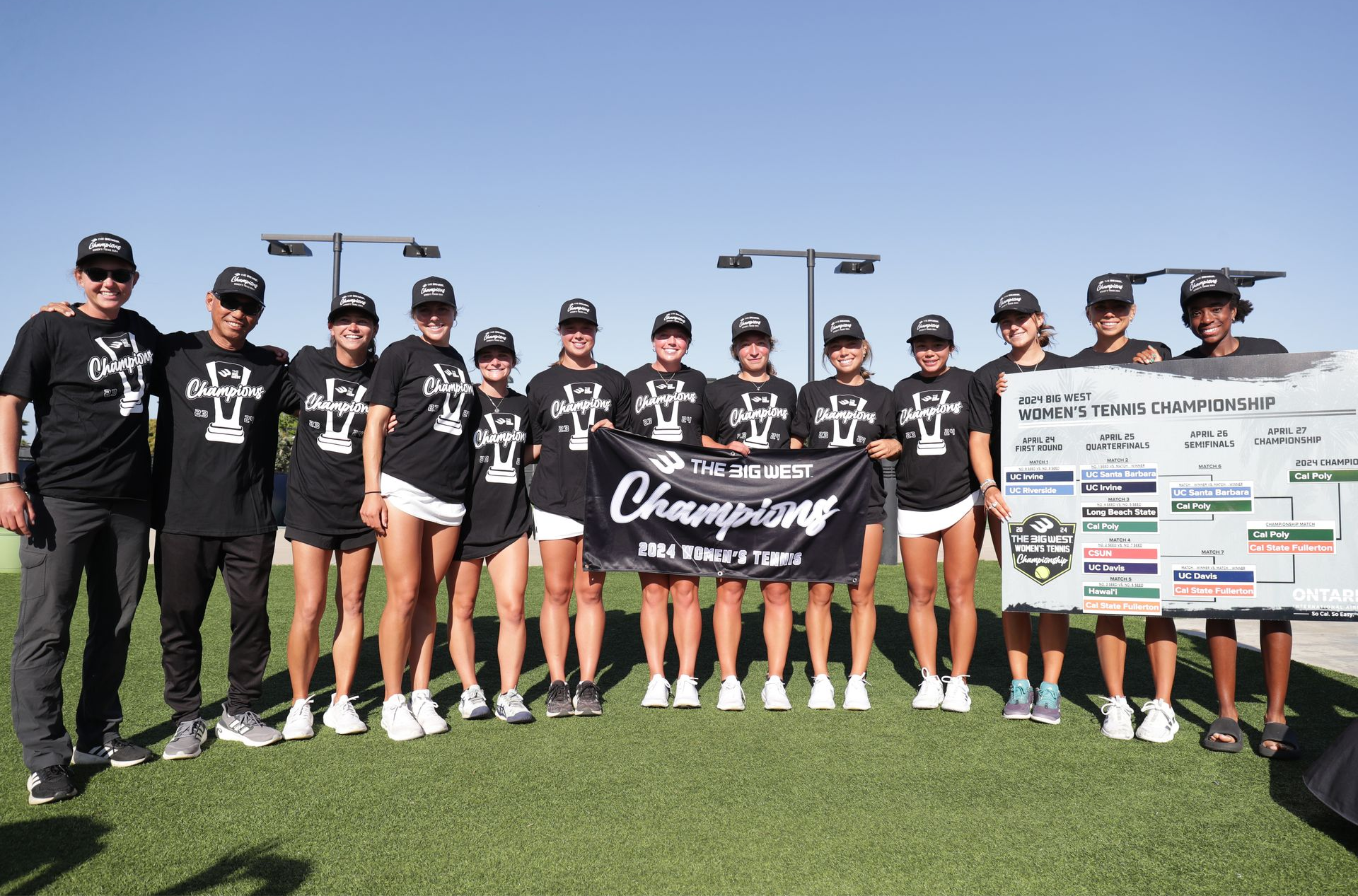 Youth softball team in black uniforms posing on a field with a championship sign and trophy
