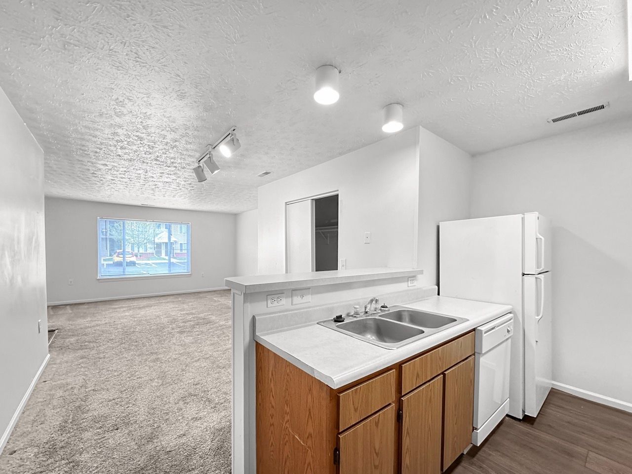 A kitchen with a sink , refrigerator , dishwasher and a window.